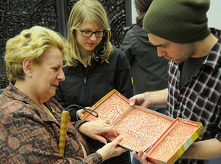 Die Studierenden Nicolas Lucker und Anja Skowronski erläutern Ingeborg Roth das Kunstwerk "Perit mundus – Fiat iustitia" von Robert Höfling, das im Hintergrund zu sehen ist. Ingeborg Roth ist blind. Foto: Gunnar Bartsch